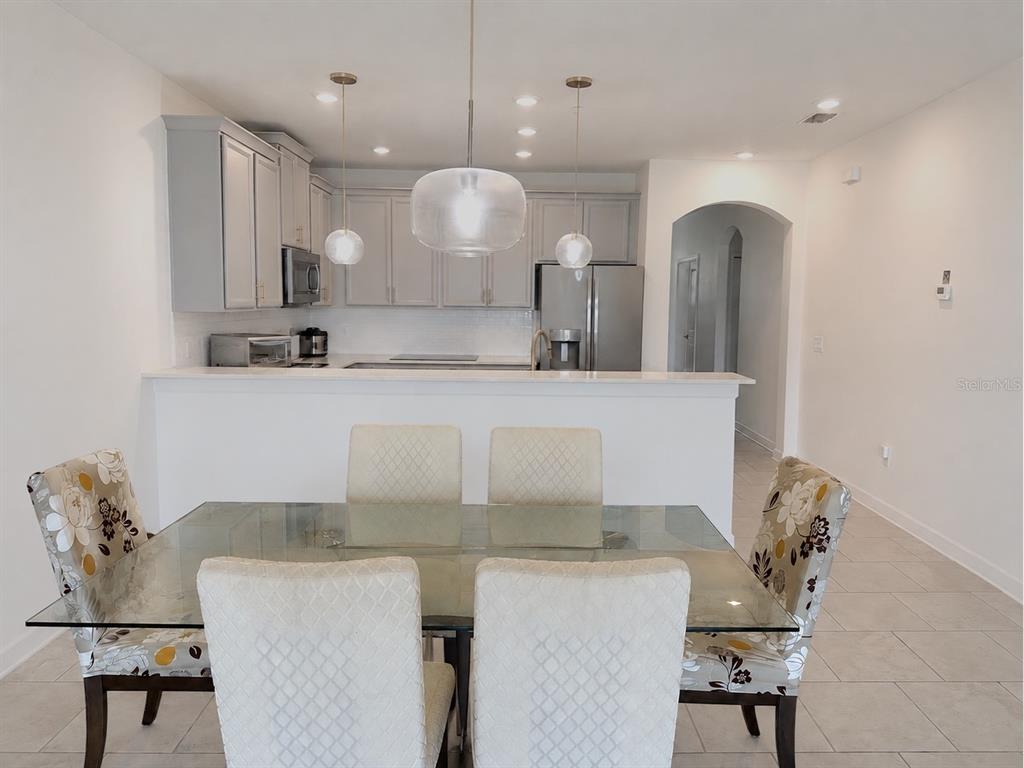 A dining area with a glass table sits in front of a kitchen with gray cabinets — 8990 AZALEA SANDS LANE, DAVENPORT, FL