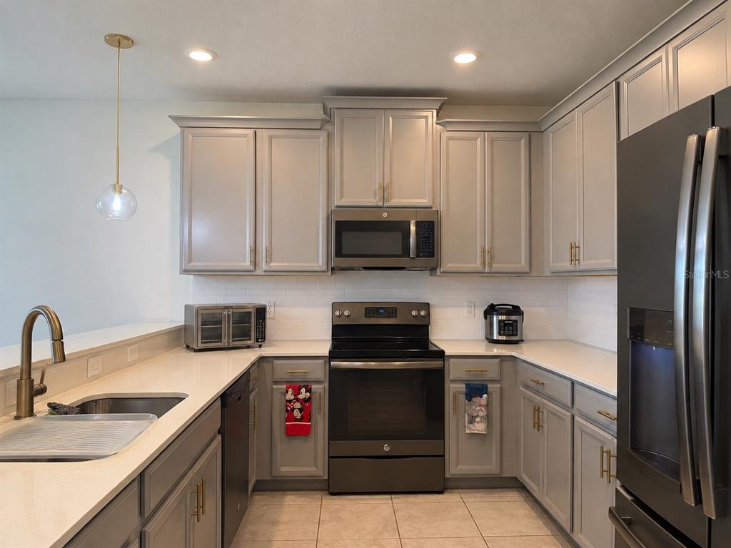 A kitchen features gray cabinets, white countertops, a black stove, and a stainless steel refrigerator — 8990 AZALEA SANDS LANE, DAVENPORT, FL