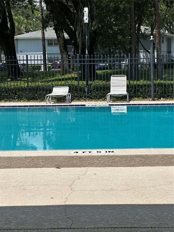 A swimming pool with two lounge chairs sits in front of a multi-story apartment building — 584 FAIRWAYS LANE UNIT F202, OCALA, FL