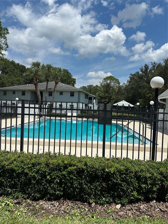 A swimming pool is enclosed by a black metal fence in front of an apartment building — 584 FAIRWAYS LANE UNIT F202, OCALA, FL