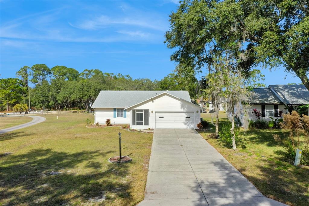 A single-story white house with a garage and a concrete driveway sits on a lawn — 1409 NEW ABBEY AVENUE, LEESBURG, FL