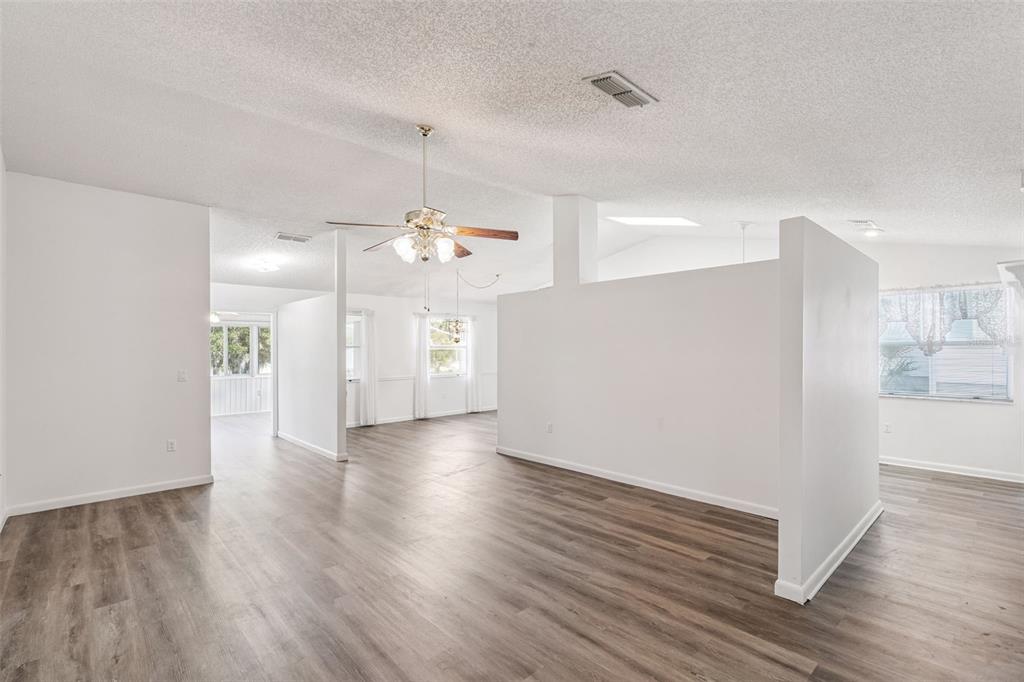 An open-concept living area features white walls, a ceiling fan, and light wood-look flooring — 1409 NEW ABBEY AVENUE, LEESBURG, FL