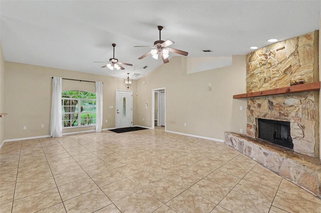 A spacious living room features tile flooring, a stone fireplace, and two ceiling fans — 4618 REOLA ROAD, DOVER, FL