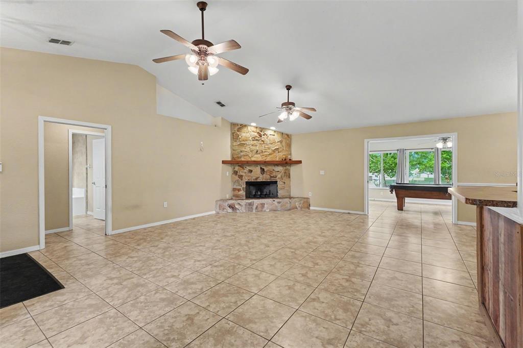 A spacious living room features tile flooring, a stone fireplace, and two ceiling fans — 4618 REOLA ROAD, DOVER, FL