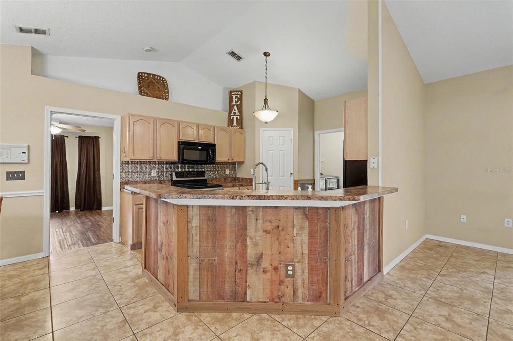 A kitchen features a rustic wood-paneled breakfast bar, light wood cabinets, and tan tile flooring — 4618 REOLA ROAD, DOVER, FL