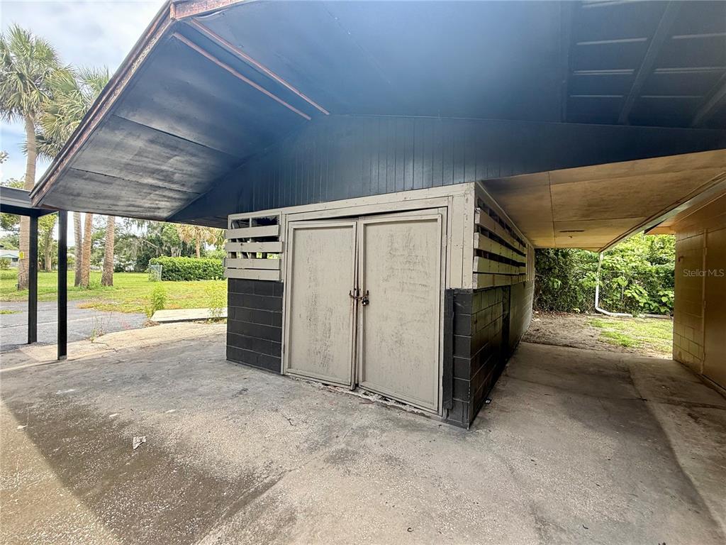 A storage shed with double doors sits under a carport on a concrete slab — PALMETTO STREET, EUSTIS, FL