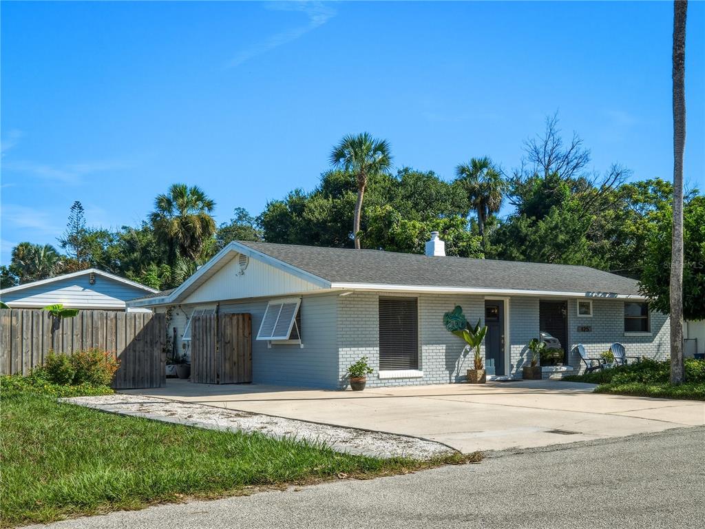 A single-story gray brick house features a concrete driveway, white shutters, and surrounding palm trees — 125 DIXWOOD AVENUE, EDGEWATER, FL