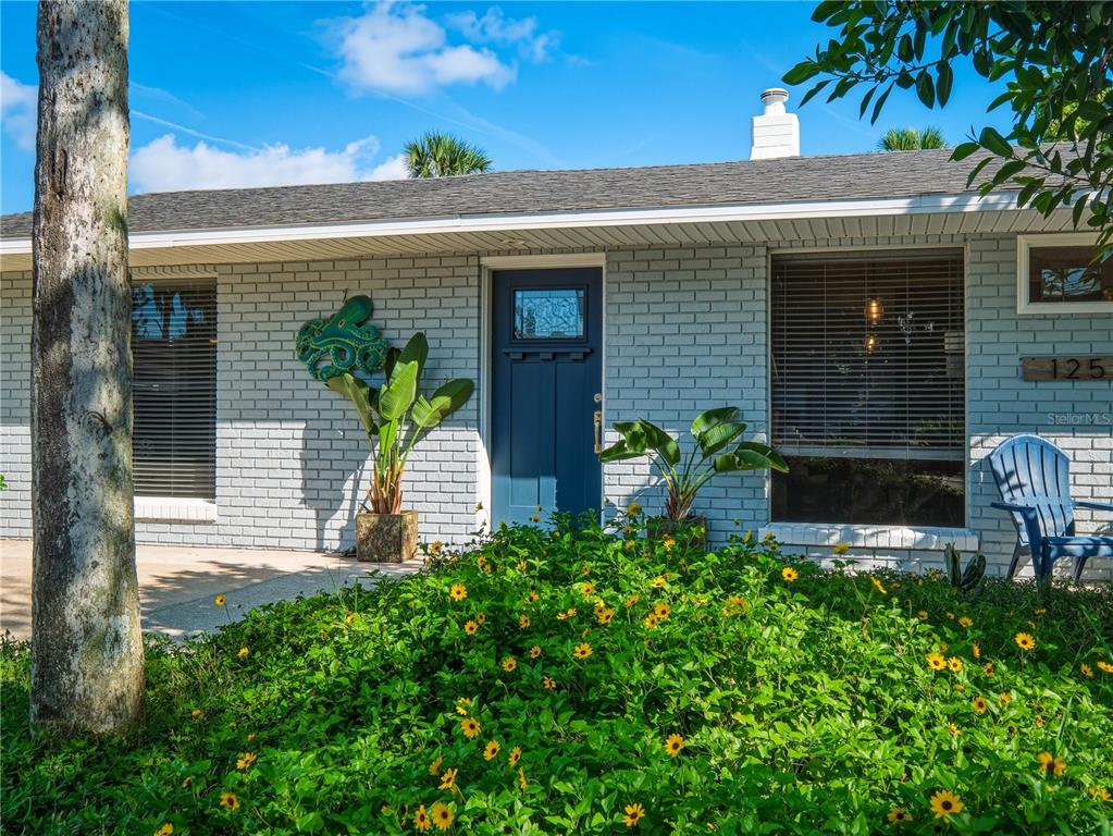 A gray brick house features a blue front door, large windows, and a yellow-flowered garden — 125 DIXWOOD AVENUE, EDGEWATER, FL