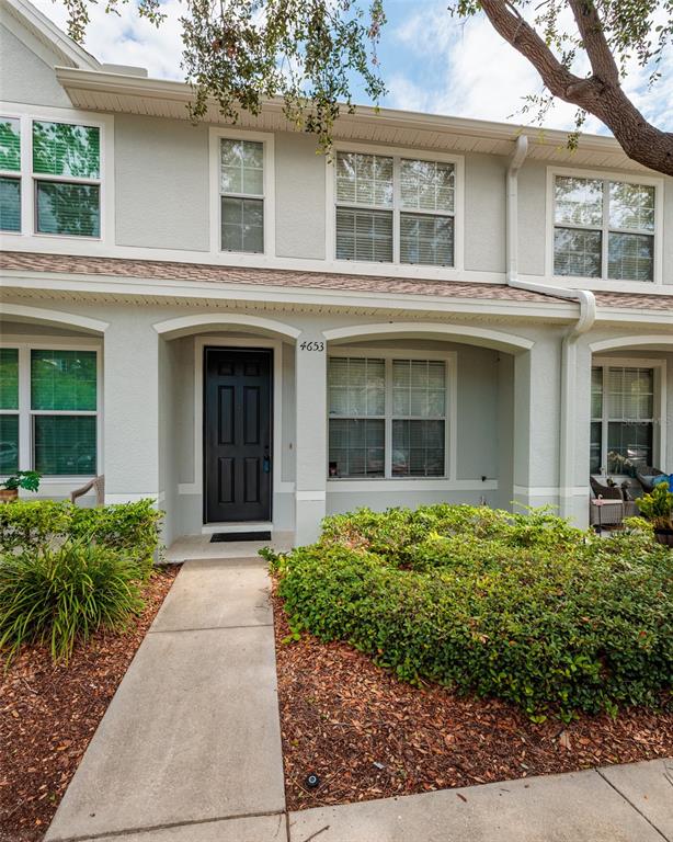 A two-story townhouse exterior features a black front door, arched entryway, and landscaped front yard — 4653 66TH PLACE N, PINELLAS PARK, FL