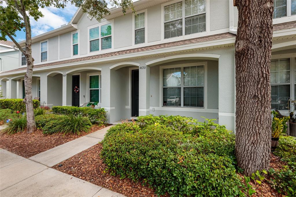 A two-story townhouse exterior with light gray siding, arched entryways, and a front garden — 4653 66TH PLACE N, PINELLAS PARK, FL