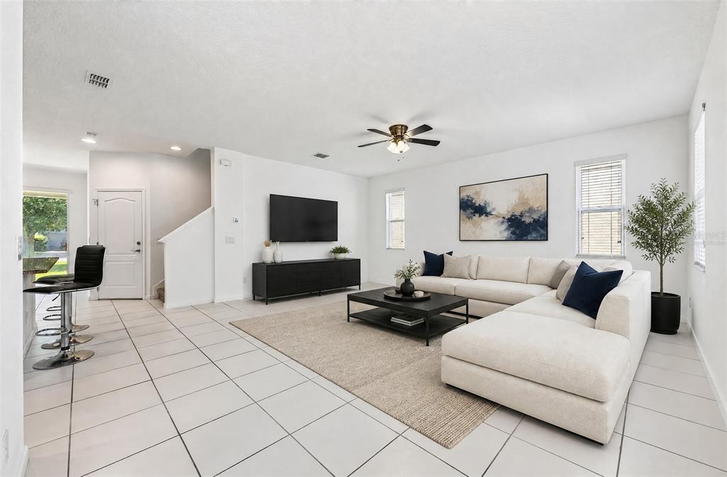 A bright living room features white walls, tile flooring, a sectional sofa, and a television — 8016 SWEET ORANGE AVENUE, WINTER GARDEN, FL