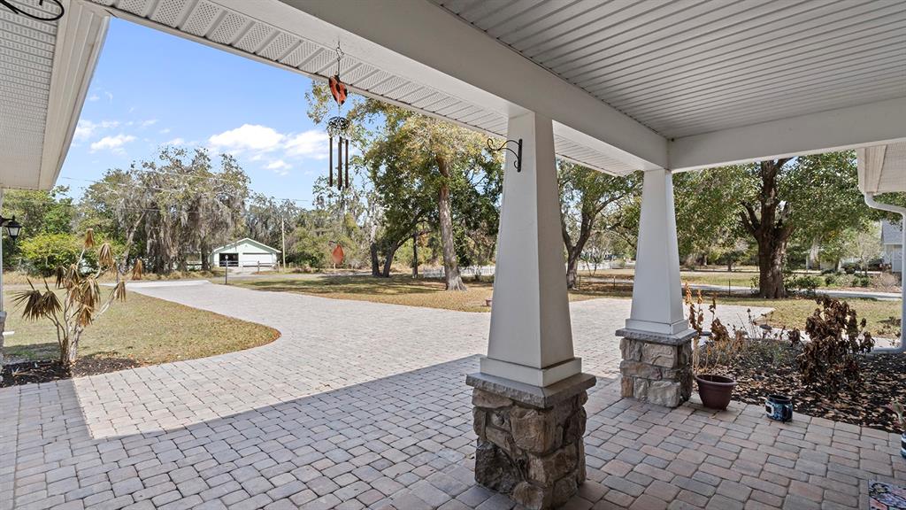 A covered stone-paved porch features white tapered columns with stone bases overlooking a yard — 4840 OLD OAK TRAIL, ST CLOUD, FL