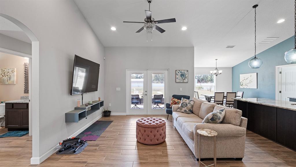 A living room features a beige sofa, pink ottoman, wall-mounted television, and wood-look tile flooring — 4840 OLD OAK TRAIL, ST CLOUD, FL