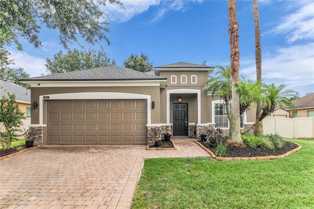 A single-story house with a brown garage, stone accents, and a paved driveway — 847 AYDEN OAK LANE, OCOEE, FL