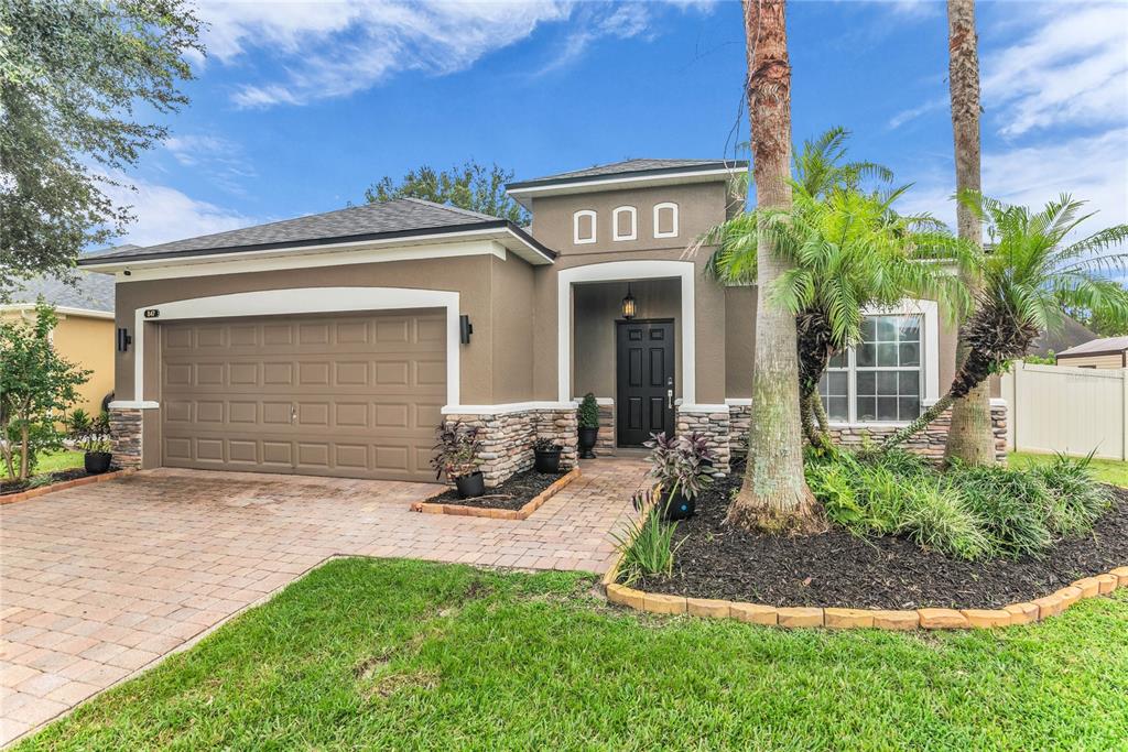 A single-story house with a tan stucco exterior, stone accents, a garage, and palm trees — 847 AYDEN OAK LANE, OCOEE, FL