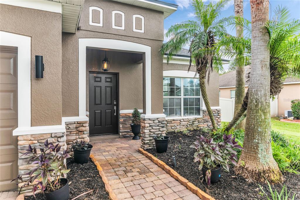 The exterior of a house features a brick walkway, stone accents, and a dark front door — 847 AYDEN OAK LANE, OCOEE, FL
