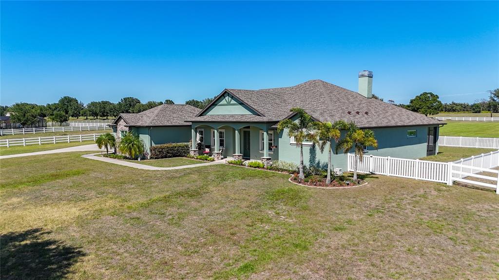 An exterior view of a green single-story house with a shingled roof and white fencing — 6130 FOXBROOK TRAIL, PARRISH, FL