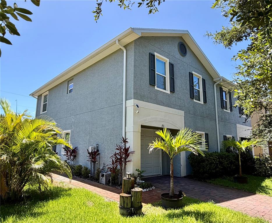 A two-story gray stucco townhouse features a covered entryway, brick walkway, and tropical landscaping — 281 ASHLEY COURT, DUNEDIN, FL
