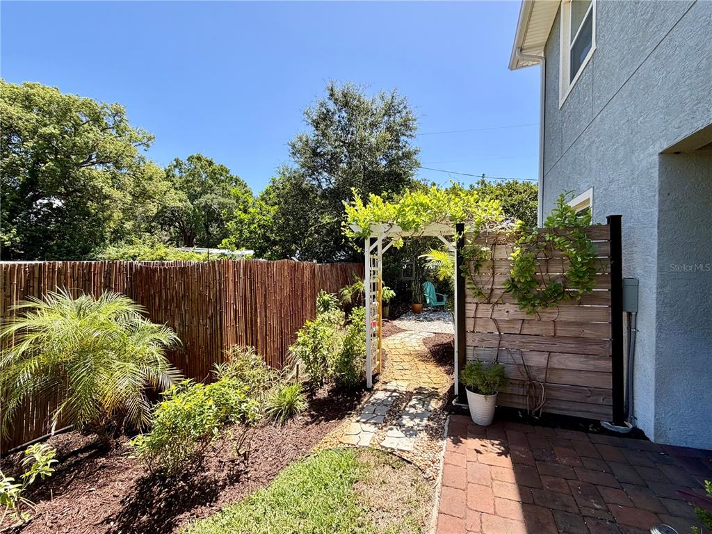 A backyard features a brick patio, a wooden fence, and a white trellis with climbing vines — 281 ASHLEY COURT, DUNEDIN, FL