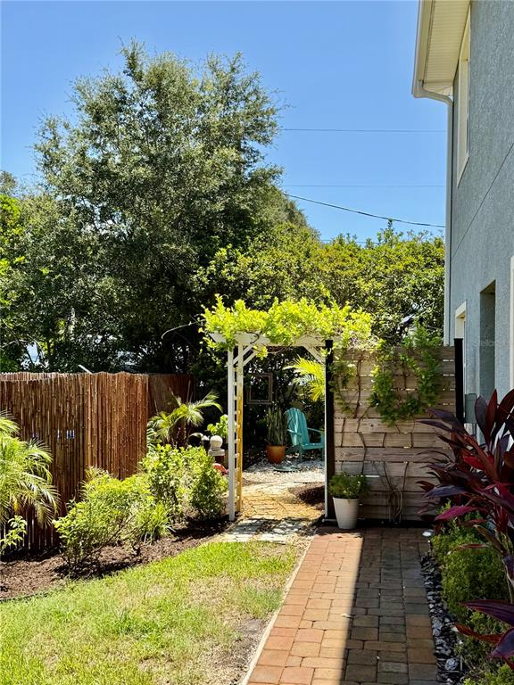 A brick walkway leads to a white wooden arbor in a landscaped backyard — 281 ASHLEY COURT, DUNEDIN, FL