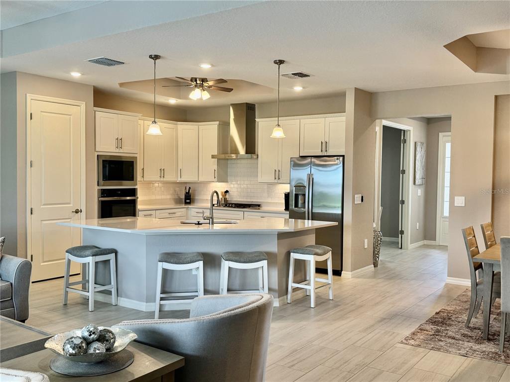 A kitchen features white cabinetry, stainless steel appliances, a large island with seating, and tile flooring — 19146 CHERRYSTONE WAY, LAKEWOOD RANCH, FL