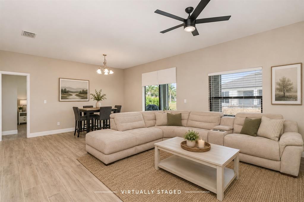 A virtually staged living and dining area with a sectional sofa, coffee table, and wood-look flooring — 2841 NW 45TH PLACE, CAPE CORAL, FL