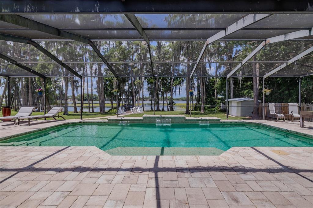 A screened-in swimming pool with water features overlooks a lake surrounded by mossy trees — 5035 CONNER DRIVE, LAND O LAKES, FL