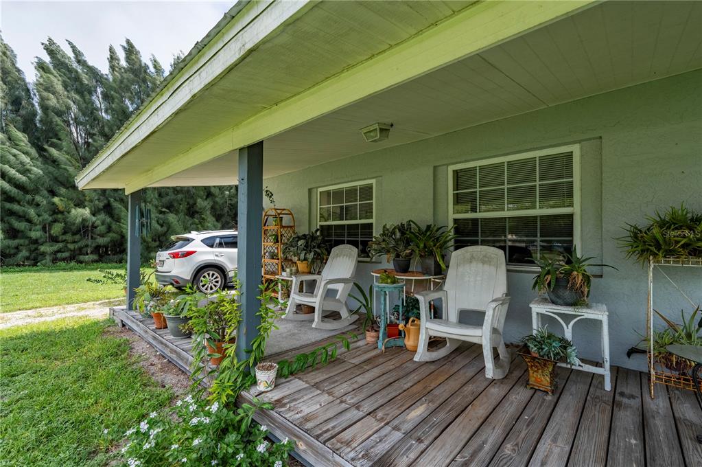 A wooden porch with two rocking chairs, potted plants, and a view of a parked car — 5380 SABAL PALM LANE, PUNTA GORDA, FL