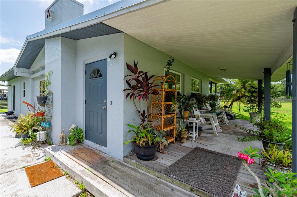 A covered wooden porch features a gray door, potted plants, and outdoor furniture — 5380 SABAL PALM LANE, PUNTA GORDA, FL