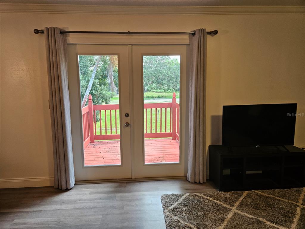 A living room features light wood-look flooring, a television on a stand, and glass doors opening to a deck — 1737 PARAKEET WAY UNIT 2, SARASOTA, FL
