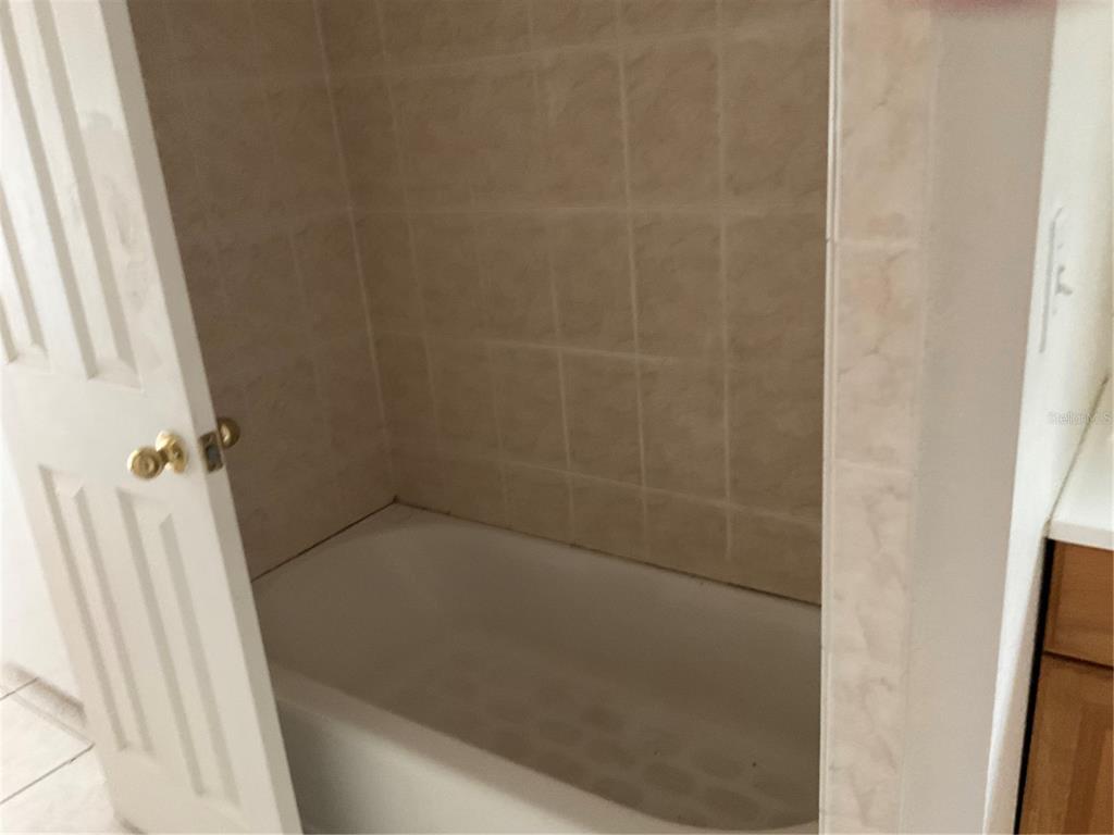 A white bathtub is surrounded by beige square wall tiles in a bathroom — 2121 LAKEVIEW DRIVE, SEBRING, FL
