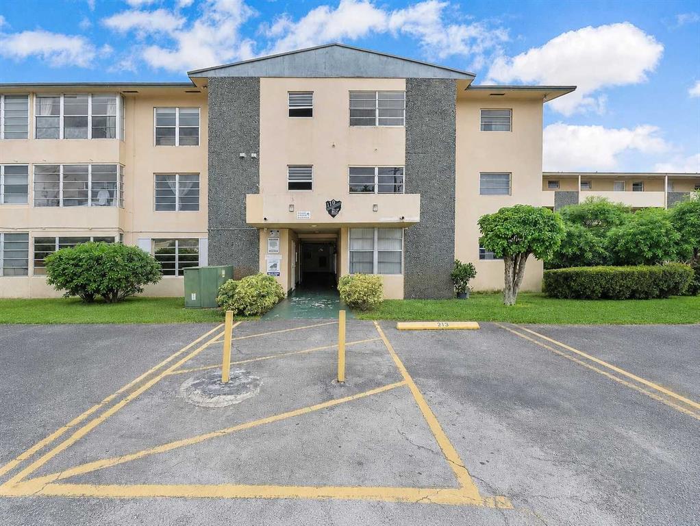 A three-story apartment building exterior with a central entrance and a paved parking lot — 110 ROYAL PALM ROAD UNIT 208, HIALEAH GARDENS, FL