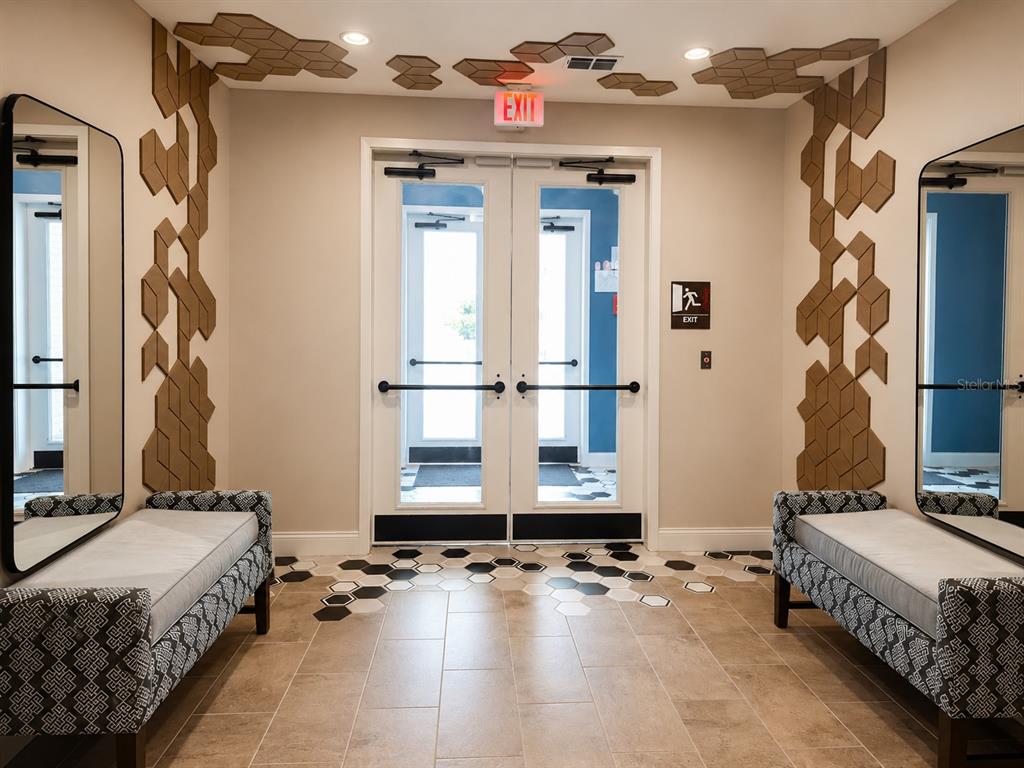 A foyer features two benches, hexagonal wall accents, and double glass doors with an exit sign — 7545 LAUREATE BOULEVARD UNIT 7208, ORLANDO, FL