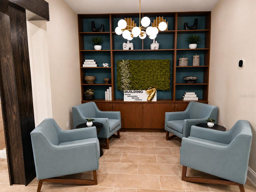 A seating area features four blue armchairs, a central bookshelf, and a moss wall accent — 7545 LAUREATE BOULEVARD UNIT 7208, ORLANDO, FL
