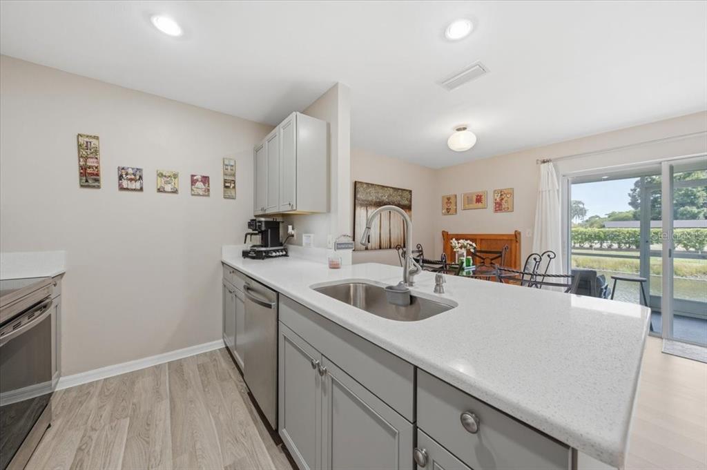 A kitchen with grey cabinets, white countertops, and a stainless steel sink overlooks a dining area — 5503 67TH AVENUE N UNIT 18, PINELLAS PARK, FL
