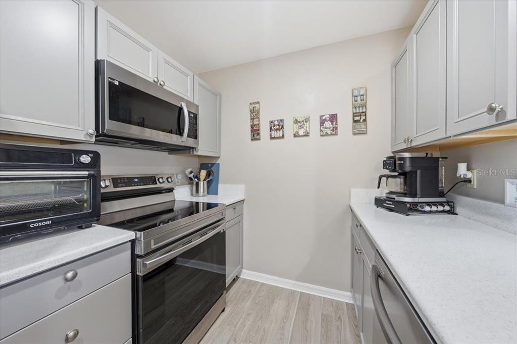 A galley-style kitchen features grey cabinets, stainless steel appliances, and light-colored countertops — 5503 67TH AVENUE N UNIT 18, PINELLAS PARK, FL