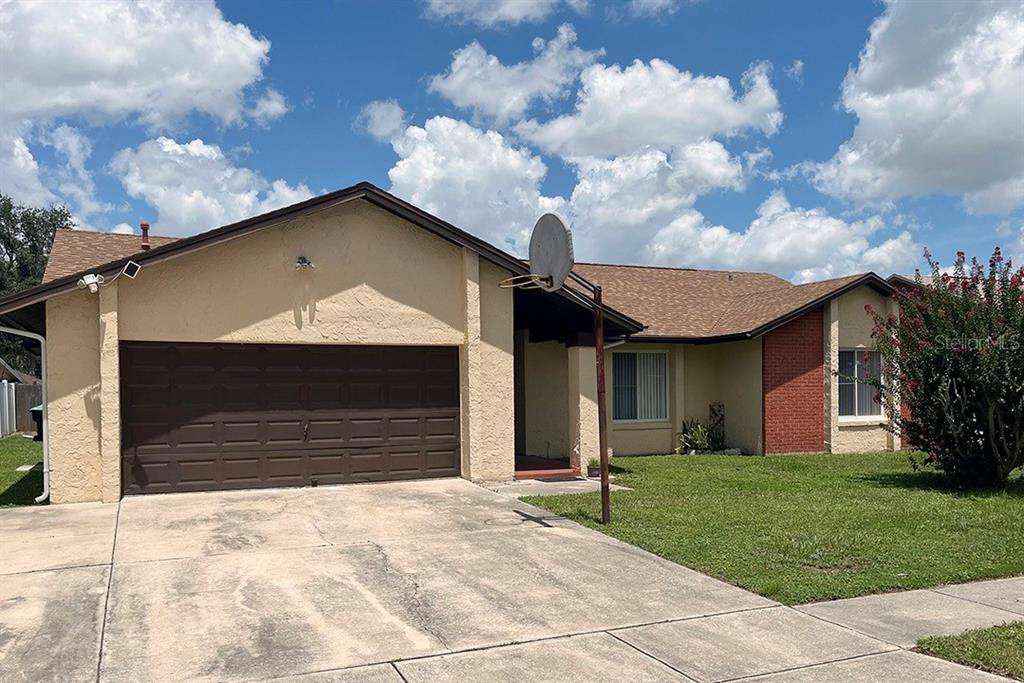 A single-story house features a tan stucco exterior, a brown garage door, and a brick accent wall — 2127 SPICE AVENUE, ORLANDO, FL