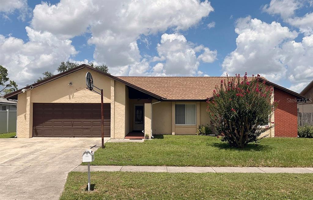 A single-story house with a tan stucco exterior, a brick accent wall, and a driveway — 2127 SPICE AVENUE, ORLANDO, FL