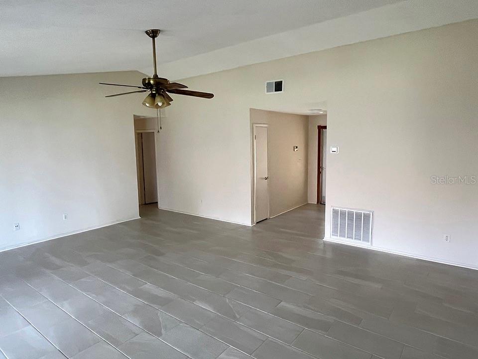A spacious room features light-colored tile flooring, a vaulted ceiling with a fan, and doorways — 2127 SPICE AVENUE, ORLANDO, FL