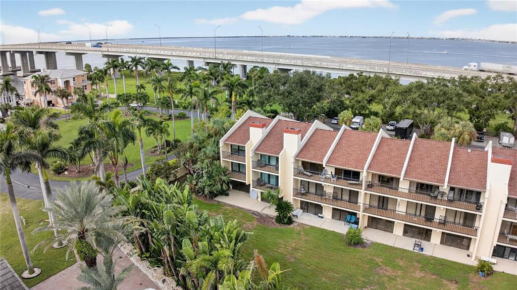 An aerial view shows a multi-story residential building with balconies near a large bridge — 7550 SUNSHINE SKYWAY LANE S UNIT P12, ST PETERSBURG, FL