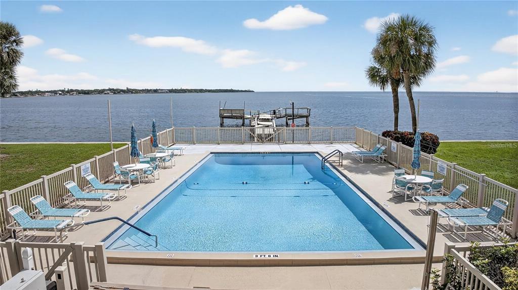 An outdoor swimming pool with lounge chairs overlooks a wooden dock on a large body of water — 7550 SUNSHINE SKYWAY LANE S UNIT P12, ST PETERSBURG, FL