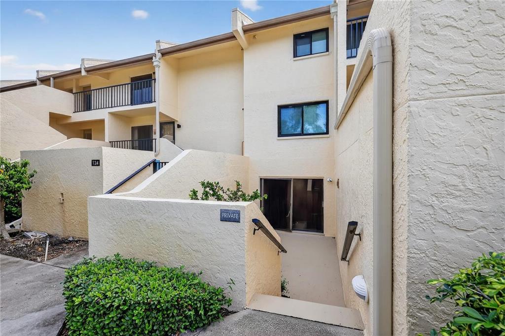 An exterior view of a multi-story stucco townhouse with a private recessed entrance and balcony — 7550 SUNSHINE SKYWAY LANE S UNIT P12, ST PETERSBURG, FL