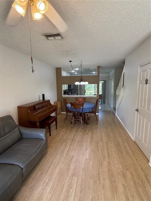 This living and dining area features wood-look flooring, a piano, and a kitchen pass-through window — 30035 GRANDA HILLS COURT, WESLEY CHAPEL, FL