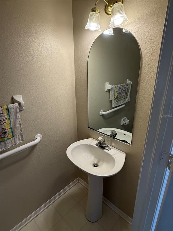 A small bathroom features a pedestal sink, an arched mirror, and wall-mounted grab bars — 30035 GRANDA HILLS COURT, WESLEY CHAPEL, FL