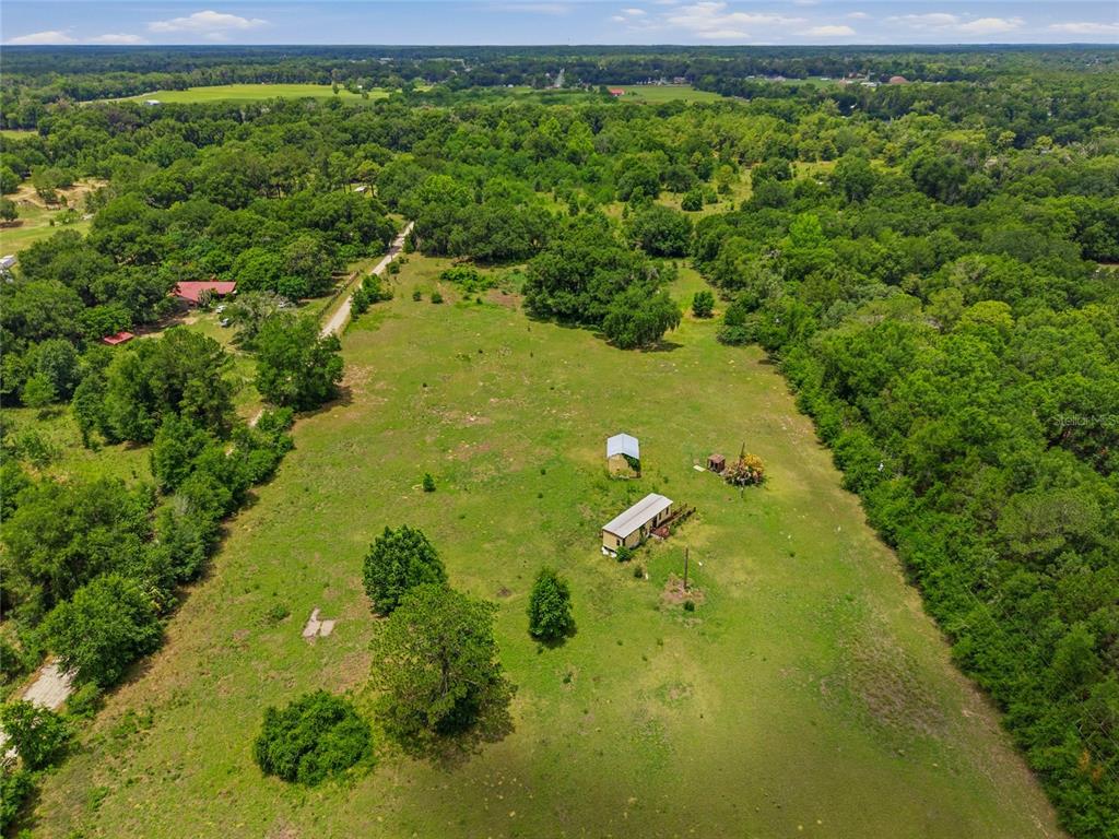 An aerial view of a grassy field containing a small house and a detached shed — 12630 U.S. 441, BELLEVIEW, FL