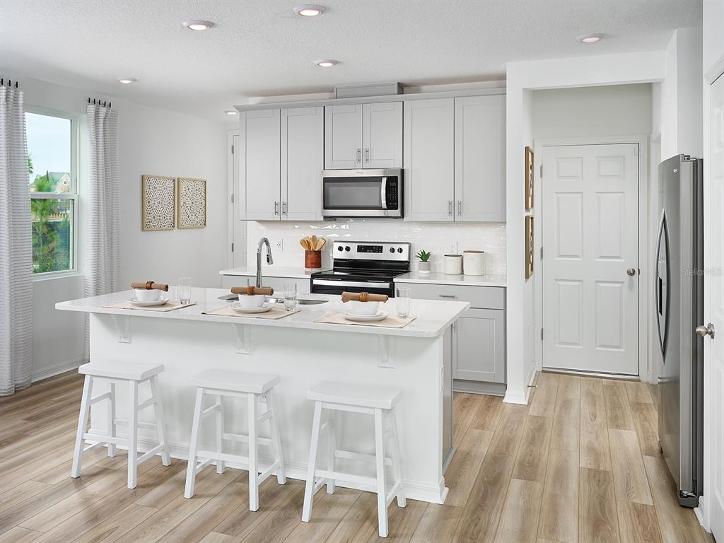 A modern kitchen features light gray cabinets, white quartz countertops, a center island, and stainless appliances — 16266 BIRD OF PARADISE AVENUE, CLERMONT, FL