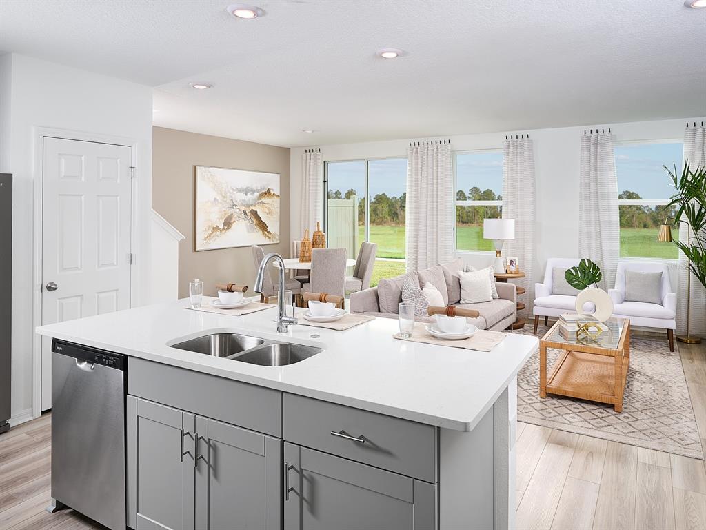 A kitchen island with a stainless steel sink overlooks an open-concept living and dining area — 16266 BIRD OF PARADISE AVENUE, CLERMONT, FL