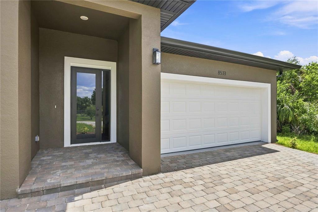 The exterior of a house features a paved driveway, a white garage door, and a doorway — 8533 LANCELOT AVENUE, NORTH PORT, FL