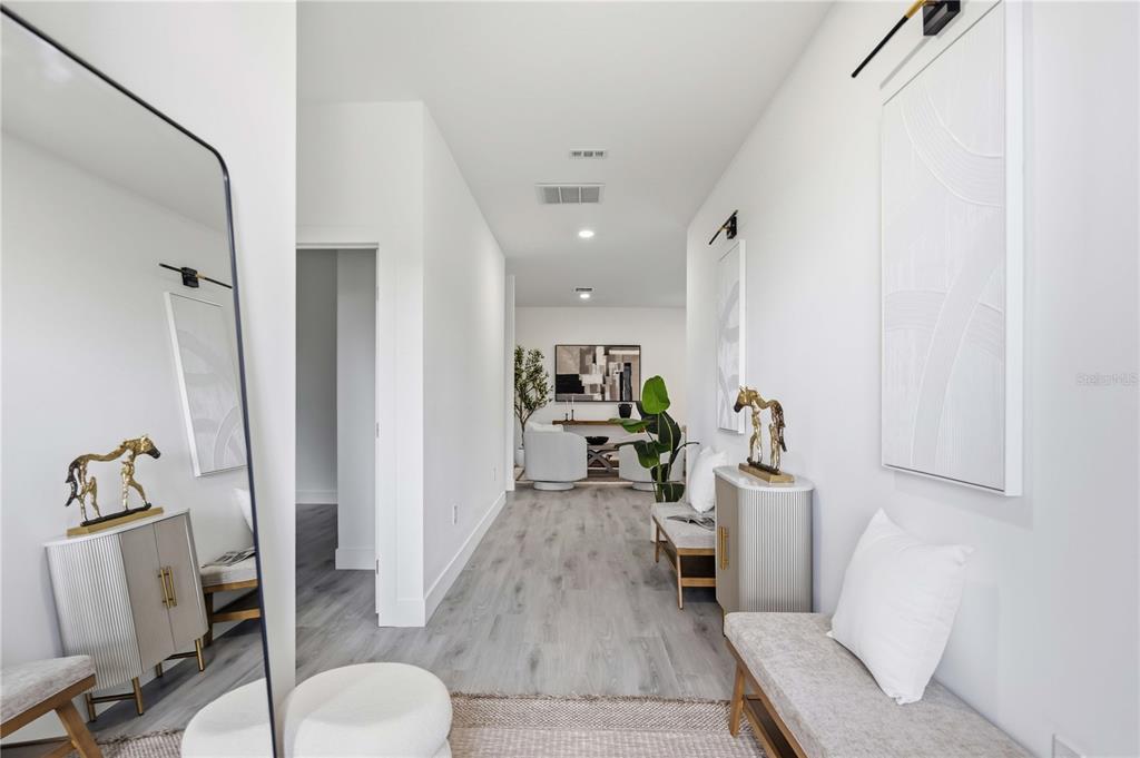 A bright hallway features light wood-look flooring, modern furniture, wall art, and a large mirror — 8533 LANCELOT AVENUE, NORTH PORT, FL