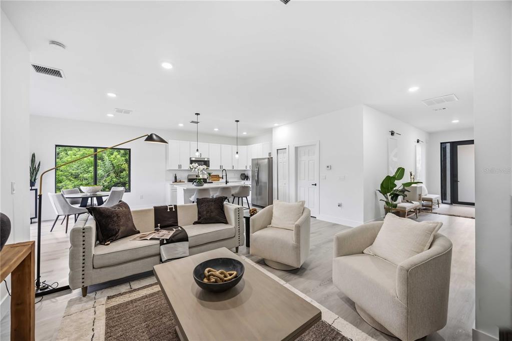 An open-concept living room and kitchen featuring white cabinetry, light wood flooring, and modern furniture — 8533 LANCELOT AVENUE, NORTH PORT, FL